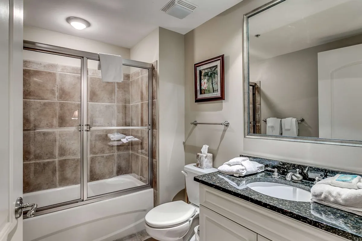 A spa-inspired interior bathroom featuring a glass shower enclosure, granite countertop, neatly arranged towels, and elegant artwork. The mood is tranquil, evoking a personal retreat ideal for unwinding after a day at the pool or fitness center.