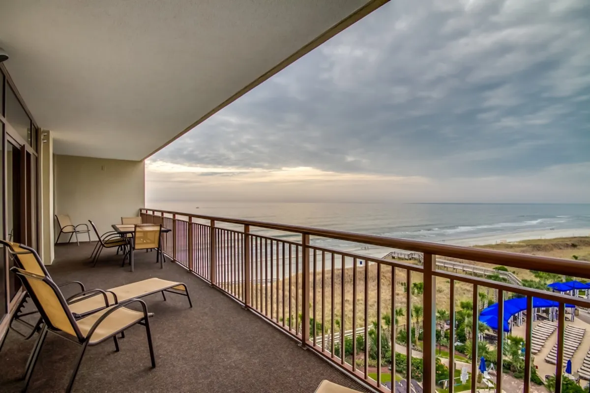 This image captures the oceanfront balcony with a clear view of the Atlantic, comfortable seating, and a serene ambiance perfect for morning coffee or sunset cocktails. The distant shoreline and cloudy sky set a tranquil, seaside mood.