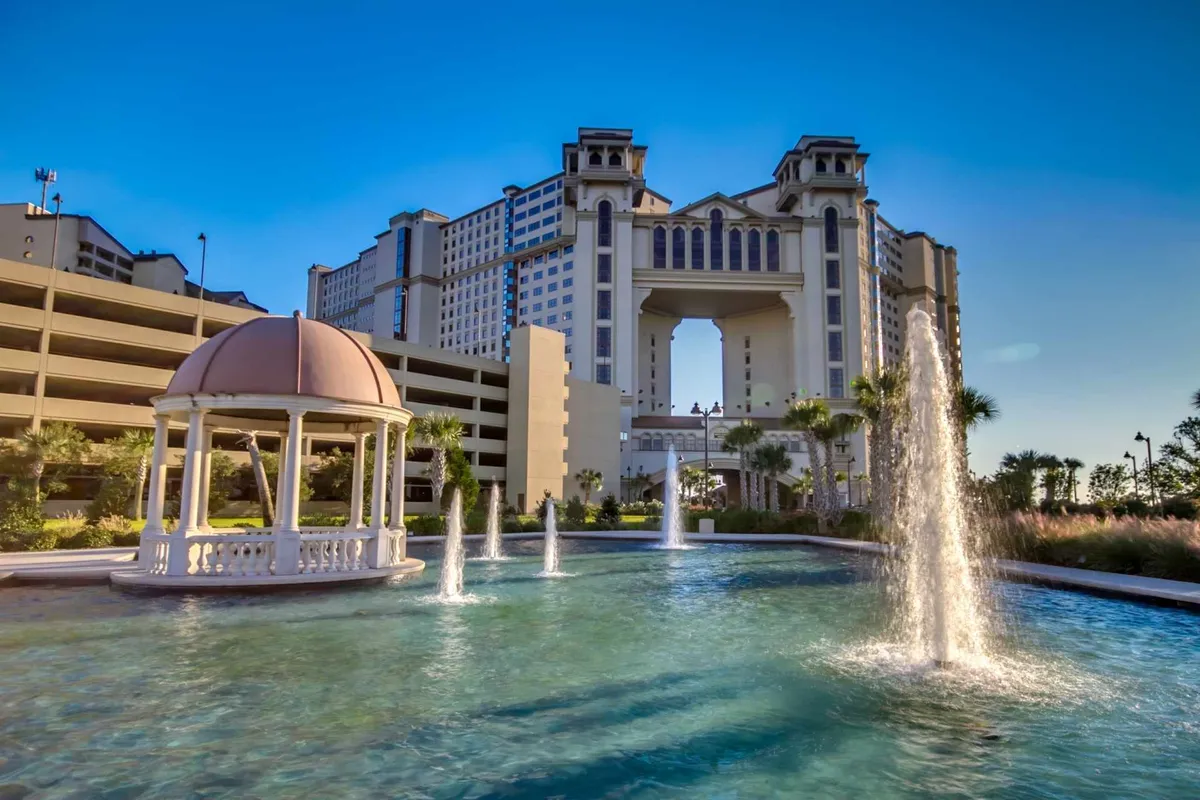 This image showcases an ornate gazebo and water fountains set against the backdrop of a large resort-style hotel structure. The setting features lush landscaping and open spaces, exuding a luxurious and serene resort atmosphere. The presence of water and outdoor gathering spaces connects directly to resort-style amenities.