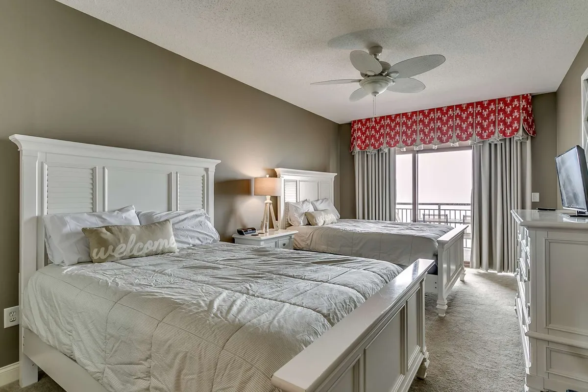 This image features a bedroom with two beds, a lamp, a dresser, and a window that lets in natural light. The atmosphere is cozy and welcoming, suitable for both resting and socializing. The view outside hints at a pleasant environment.
