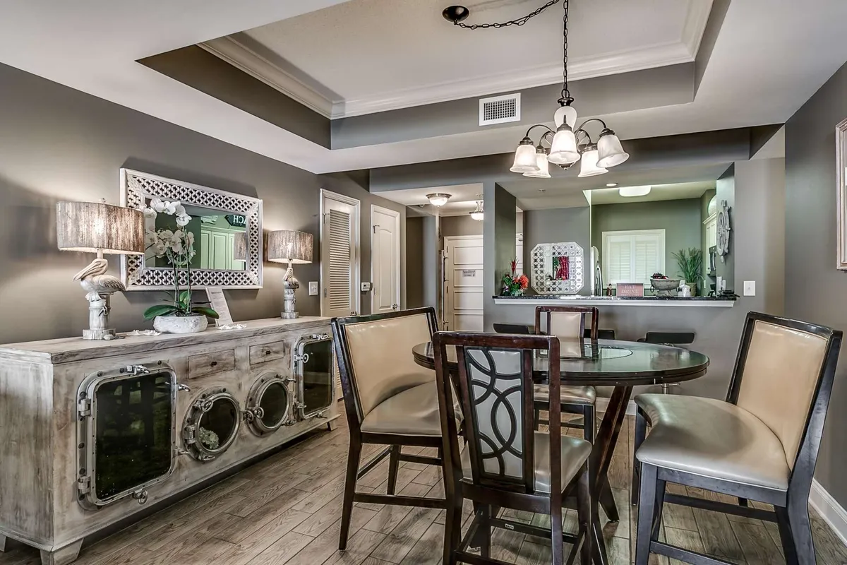 A welcoming dining area with a stylish table, a sideboard topped with decor, a large decorative mirror, and soft lighting from hanging fixtures. The setup encourages group meals and social gatherings, capturing the spirit of togetherness.
